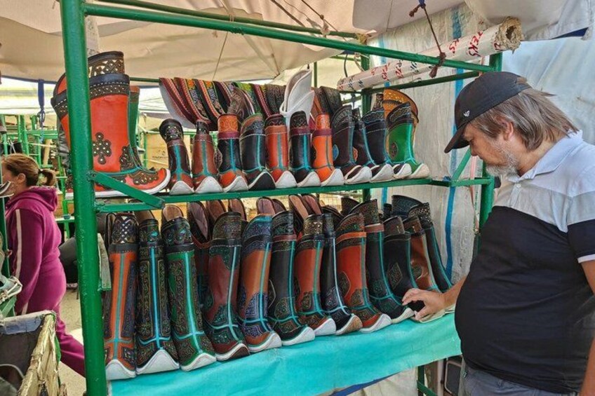 A person examining a variety of colorful boots displayed on a green rack at a market. 4