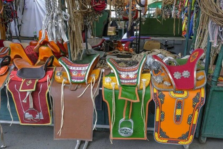 A variety of colorful leather saddles displayed at a market stall. 2