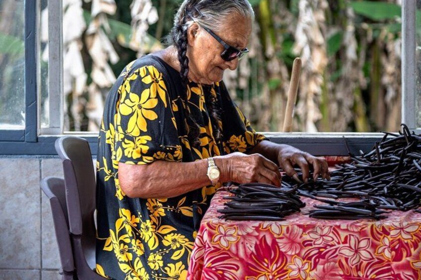 An elderly woman sorting black objects on a table with a floral tablecloth. 2
