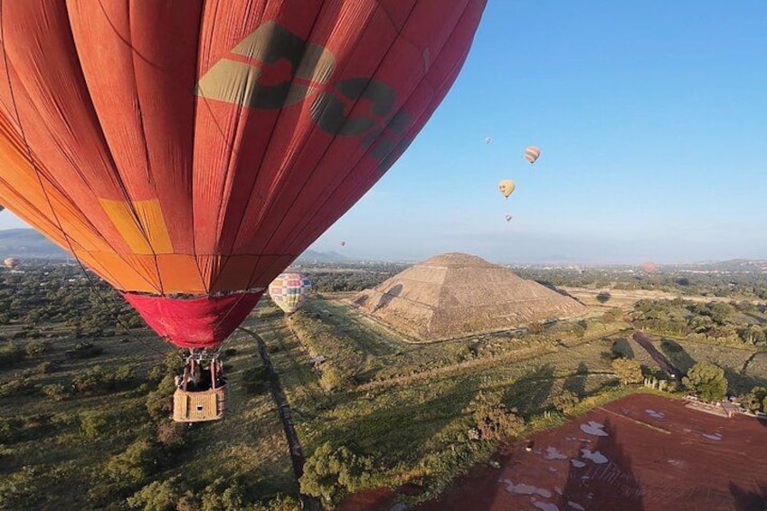 A hot air balloon over a hilly landscape with a pyramid-like structure in the distance. 1