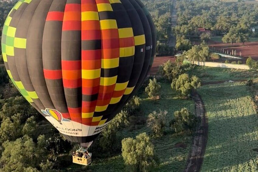 A hot air balloon with a colorful pattern flying over a rural landscape with fields and trees. 3