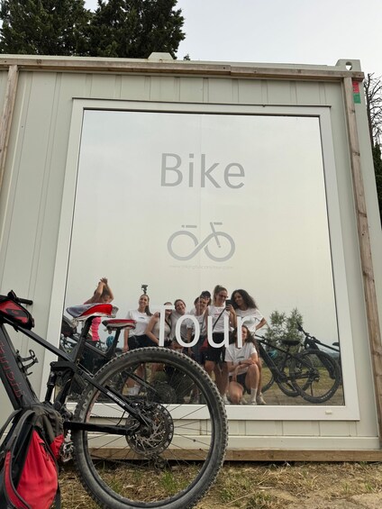 A billboard with a group of people posing in front of it, a bicycle, and a red bag on the ground. 3
