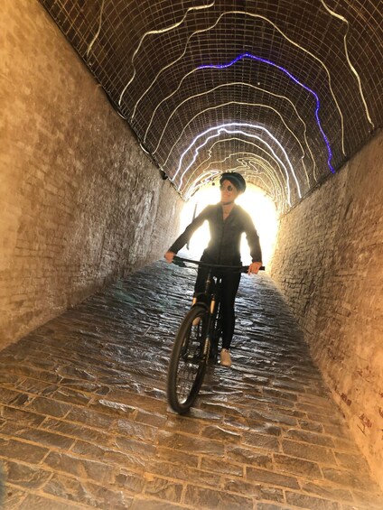 A person riding a bicycle in a stone tunnel with illuminated lines on the ceiling. 4