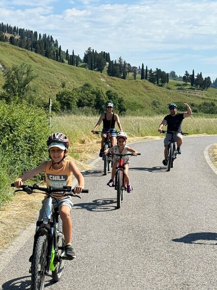 A group of cyclists on a paved road with grassy hills and trees in the background. 2