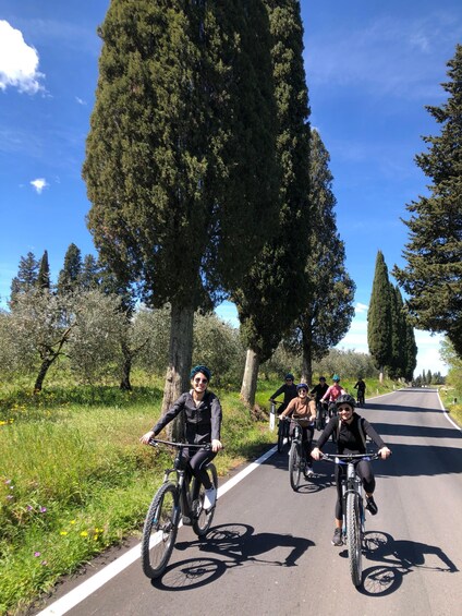 A group of cyclists on a paved road surrounded by tall trees and greenery. 5