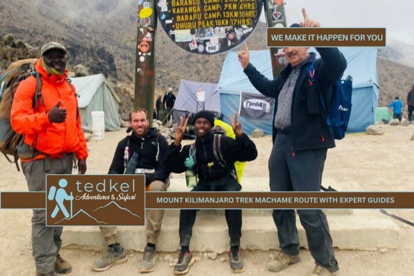 A group of hikers at a mountain campsite with tents and a signpost. 5