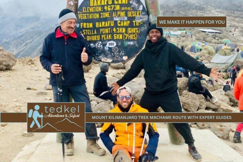 A group of people at a mountain campsite with tents and a signboard. 3