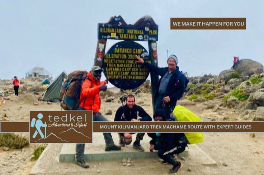 Three people standing in a rocky outdoor area with a signpost. 4