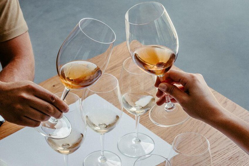 A person holding a wine glass with a light amber liquid, and another person holding a similar glass. 4