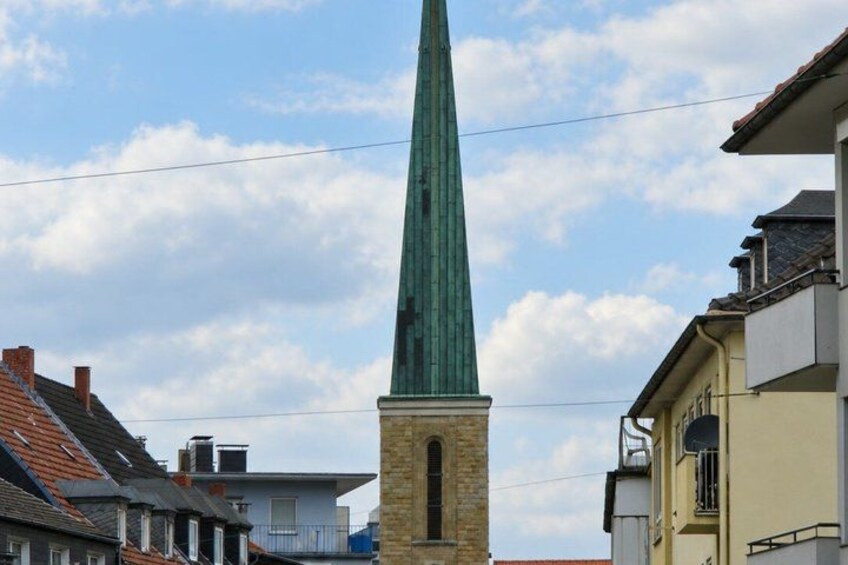 A green spire of a church with a brick base, surrounded by residential buildings. 4
