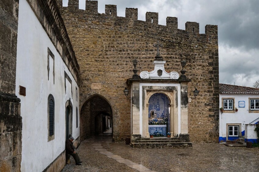 A historic stone gate with a decorative archway, a cobblestone pathway, and a building with a blue and white facade. 3
