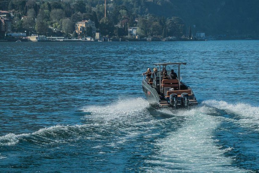A boat speeding across a calm lake with buildings in the background. 1