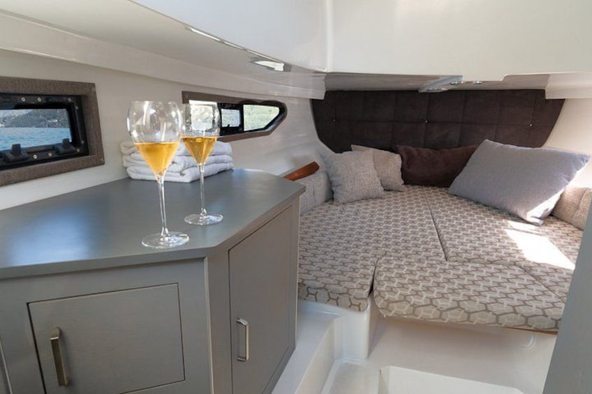 A cozy interior with a cushioned seating area, a small table with glasses, and a window overlooking water. 4