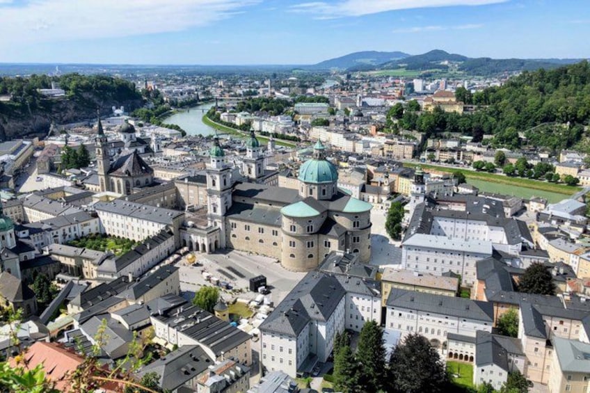 An aerial view of a historic city with a prominent church, a river, and surrounding greenery. 1