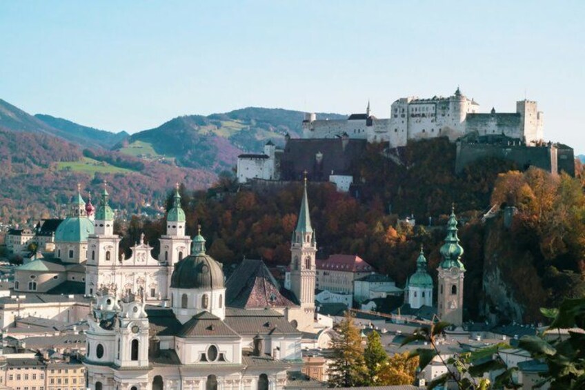 A historic city with a prominent castle on a hill, surrounded by lush autumn foliage. 3