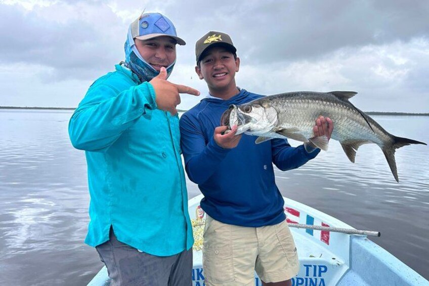 Two people holding a fish on a boat with calm water and a cloudy sky in the background. 1