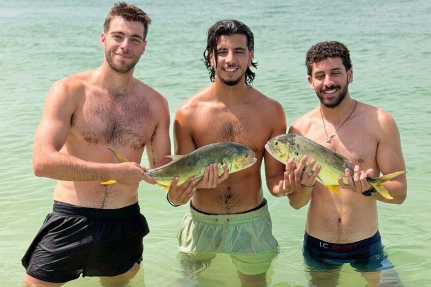 Three men holding fish in shallow water. 4