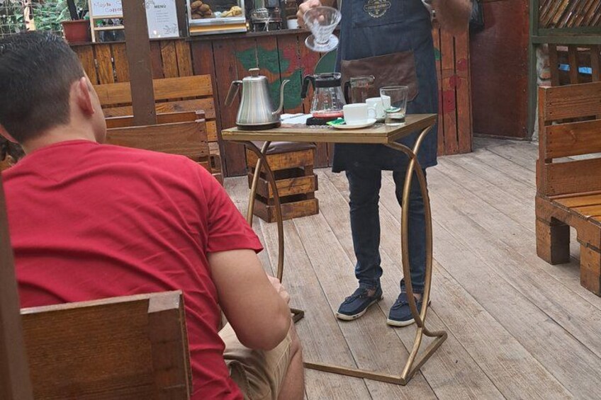 A wooden deck with a table set for two, a coffee pot, cups, and a menu board. 3