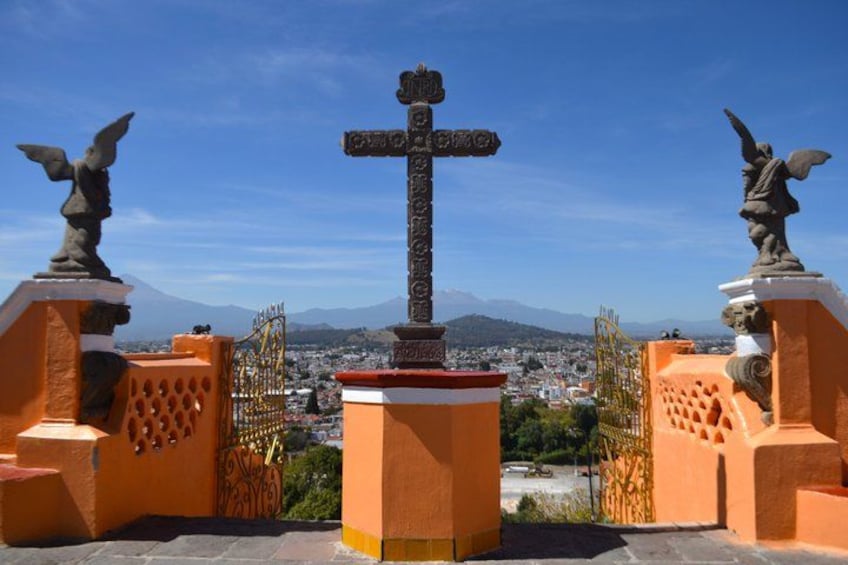 A cross monument with statues on either side, overlooking a cityscape with mountains in the background. 1