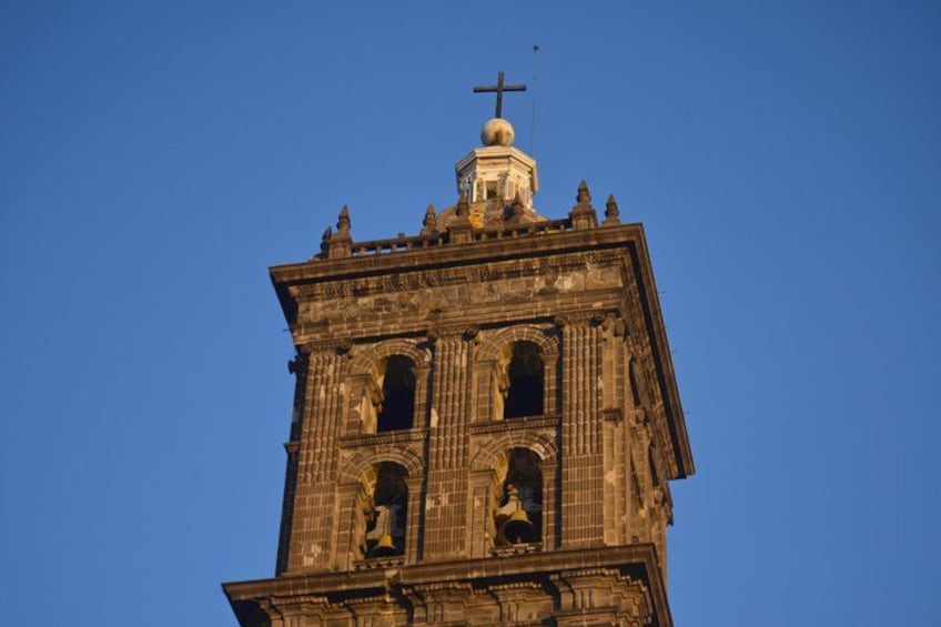 A tall, ornate tower with a cross on top, featuring intricate architectural details and multiple arched openings. 5