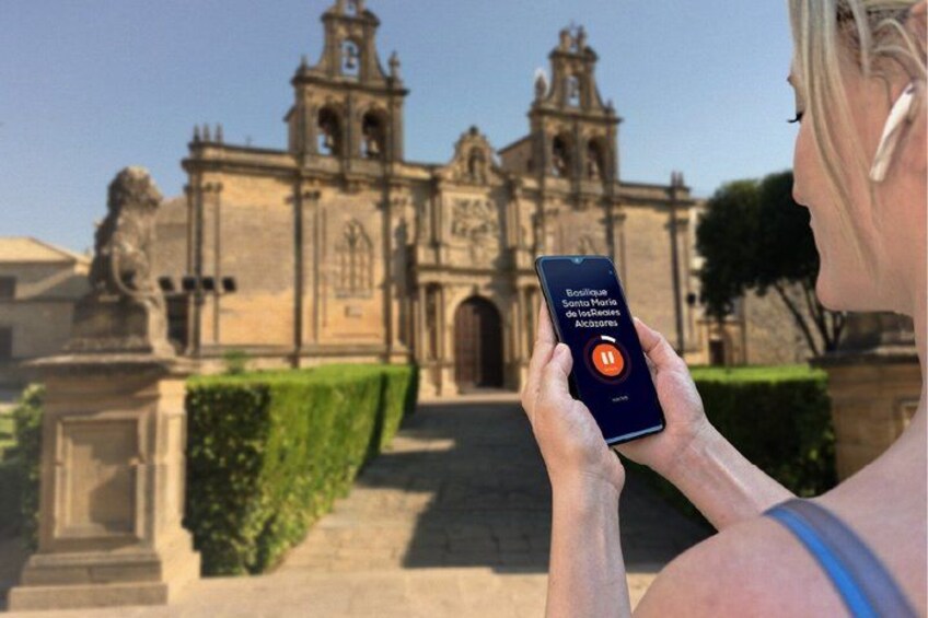 A person holding a smartphone with a map application, standing in front of a historic building with a bell tower. 5