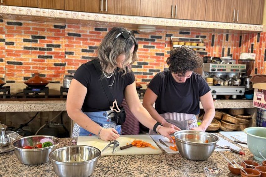 Two people preparing food in a kitchen with a brick wall and various cooking utensils. 3