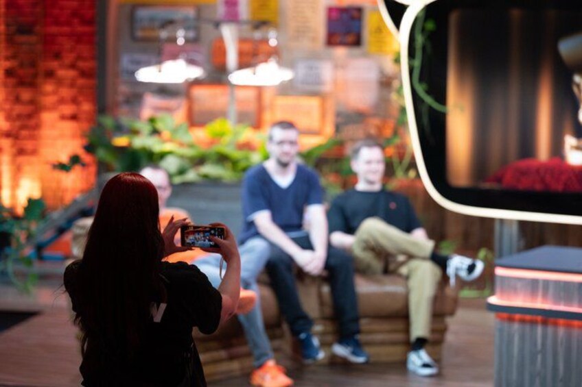 A person taking a photo with a smartphone, a group of people sitting on a couch, and a mirror reflecting part of the scene. 1