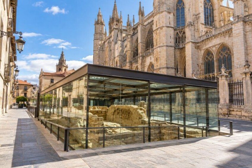 A glass enclosure with historical artifacts, a cathedral in the background, and a paved walkway. 2
