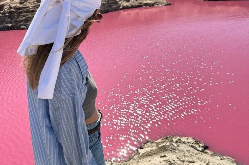 A person standing by a pink body of water with white objects floating on the surface. 5