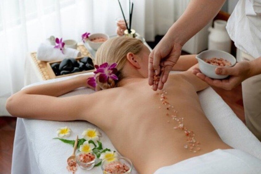 A person receiving a massage with flowers and a bowl of pink stones on their back. 3