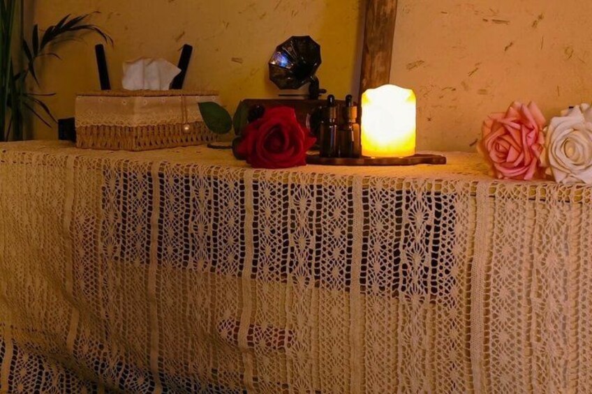 A table with a lace tablecloth, a lit candle, and two artificial roses. 4