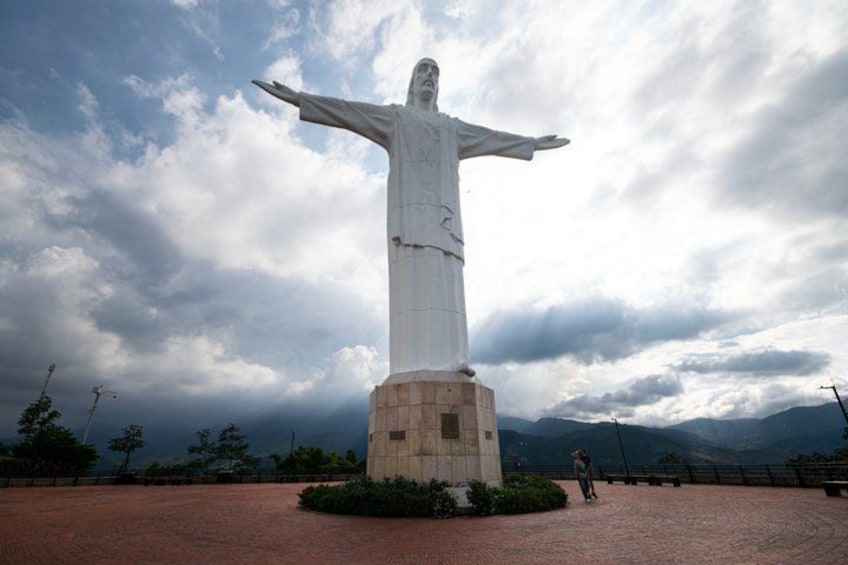 A large white statue with outstretched arms, set on a brick pedestal in an open area with mountains in the background. 2