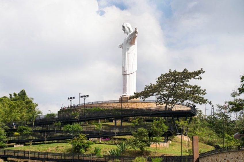 A large white statue on a platform with a bridge and surrounding greenery. 3