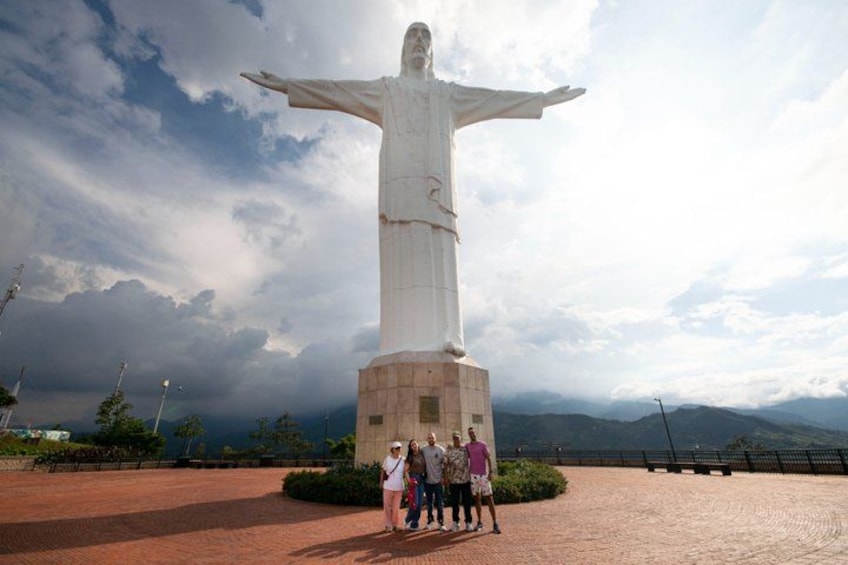 A large statue with outstretched arms, surrounded by a paved area with a few people standing nearby. 1