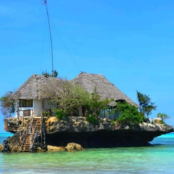 A thatched-roof house on a rocky outcrop surrounded by clear blue water. 1