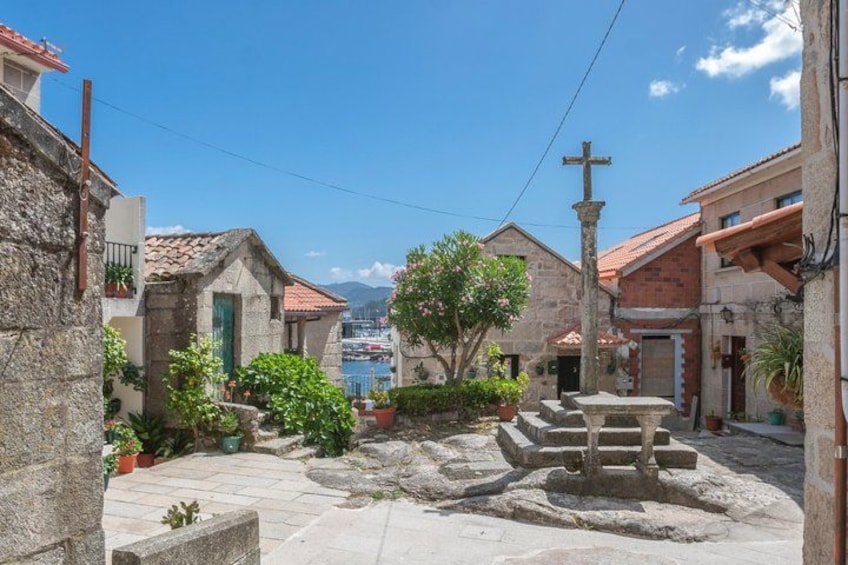 A stone courtyard with buildings, a fountain, and a cross. 4
