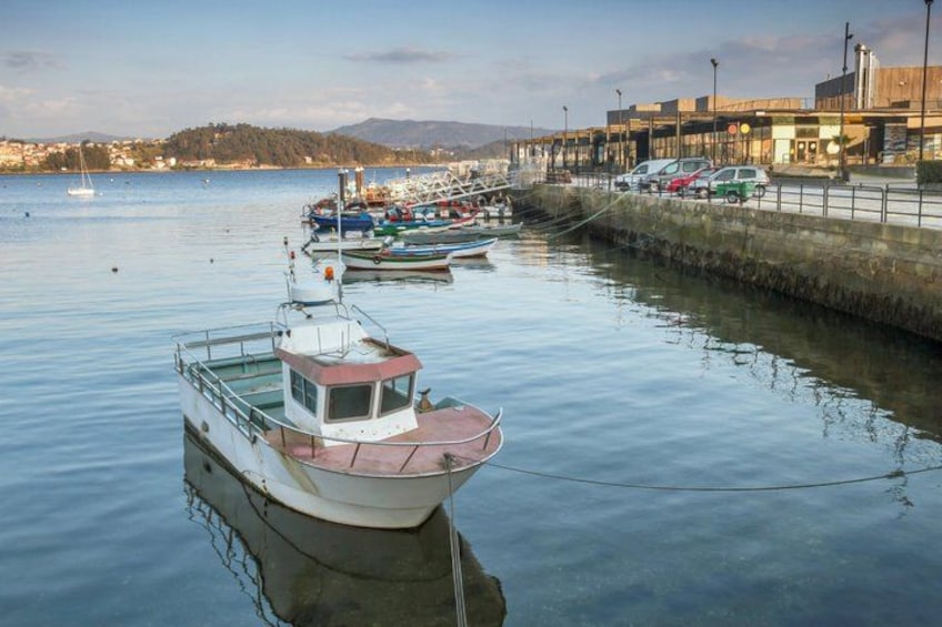 A calm harbor with boats docked along the waterfront, a bridge in the background, and a cityscape with buildings and cars. 1