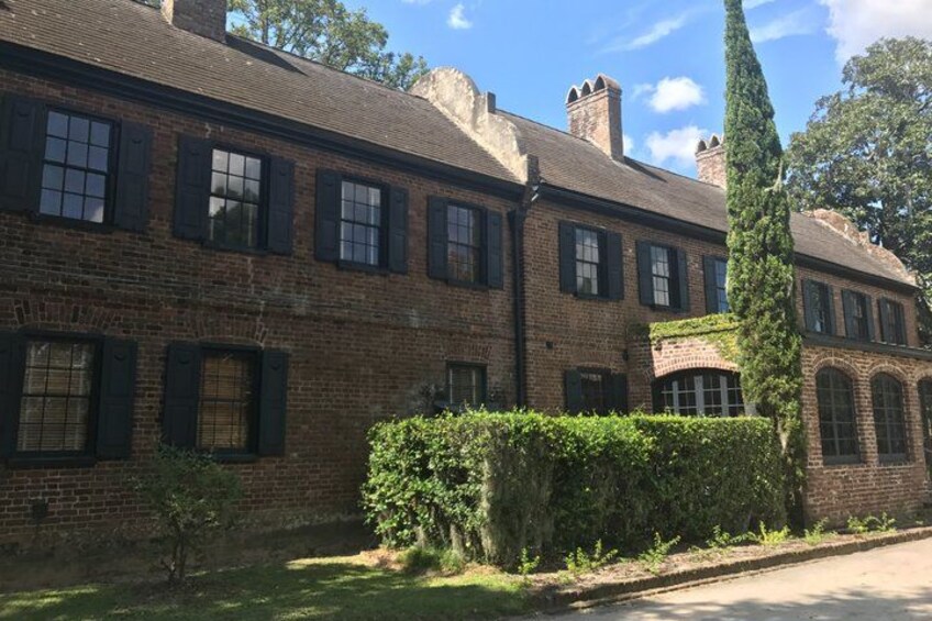 A brick building with multiple windows and a hedge in the foreground. 1