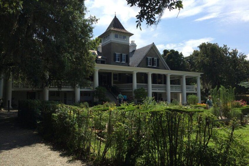 A large house with a tower, surrounded by lush greenery and a well-maintained garden. 4