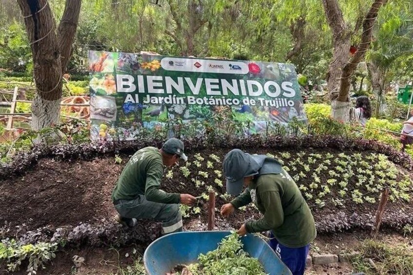 Two people working in a garden with a sign that reads 'BIENVENIDOS Al Jardín Botánico de Trujillo'. 3