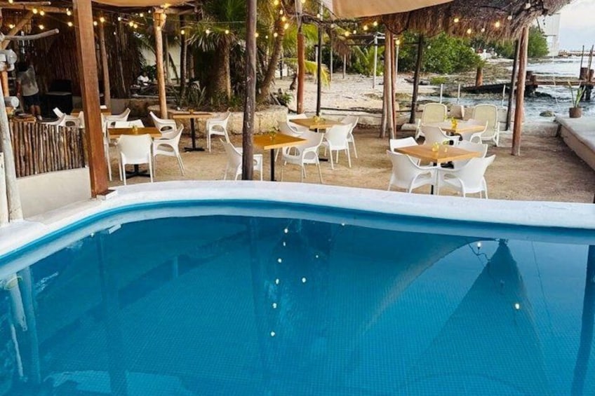 A swimming pool with white chairs and tables, surrounded by a covered area with string lights. 3