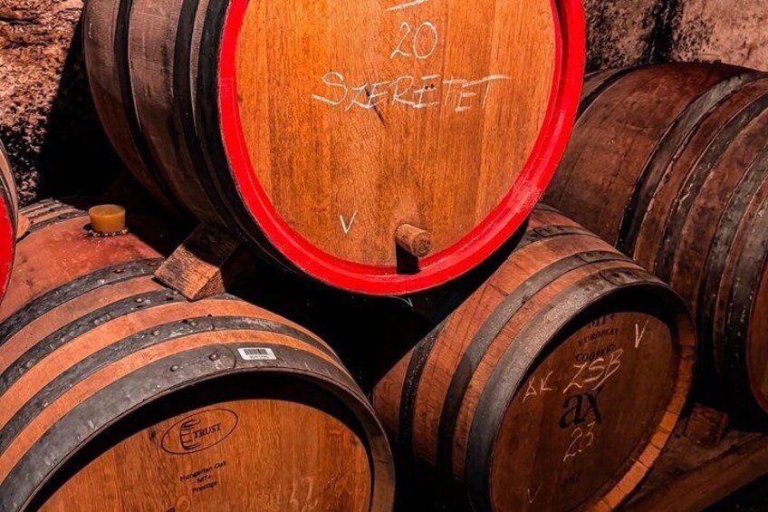 Wooden wine barrels with red stoppers, stacked closely together. 3