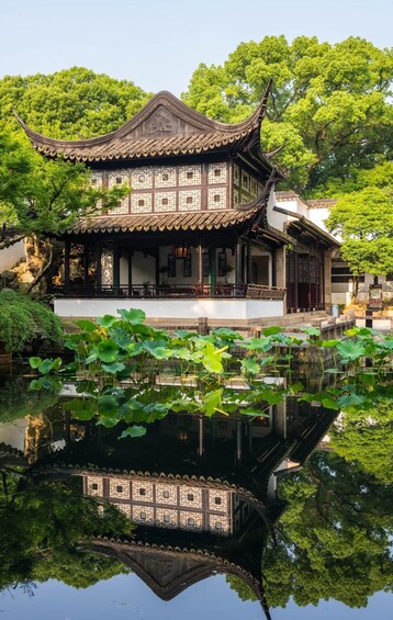 A traditional Chinese building with a tiled roof and intricate lattice windows, surrounded by lush greenery and a calm pond with lotus flowers. 1