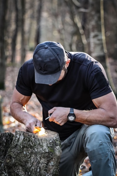 A person sitting on a tree stump in a forest, holding a lighter and a piece of wood. 1