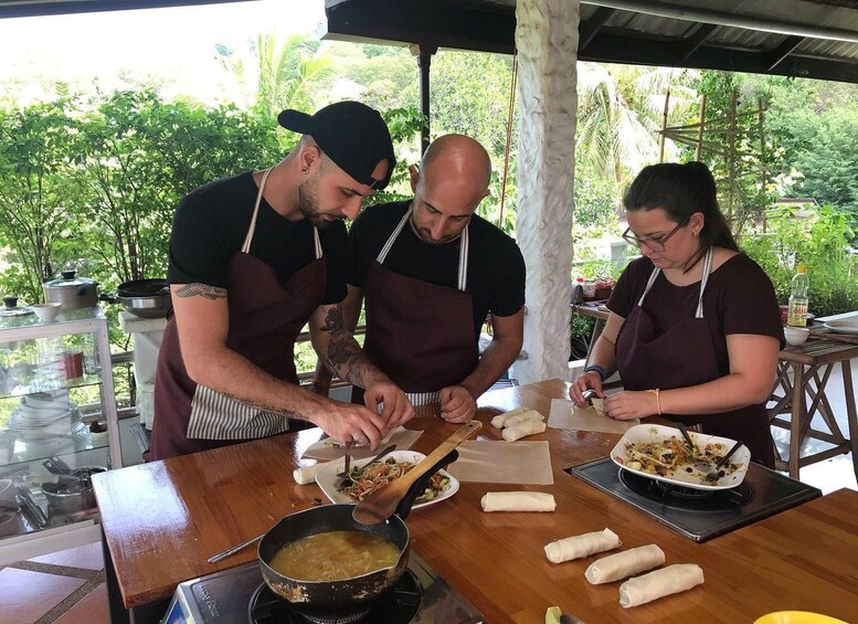 Three people preparing food outdoors, with a table full of ingredients and cooking utensils. 3