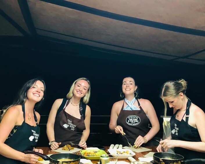 Four people wearing aprons with text, cooking at a table with various dishes and cooking utensils. 5