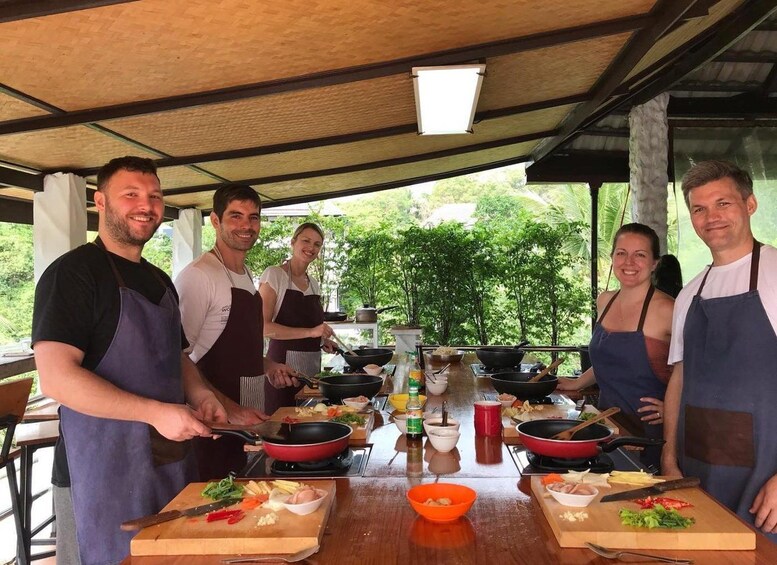 A group of people cooking outdoors with a table full of ingredients and cooking utensils. 1