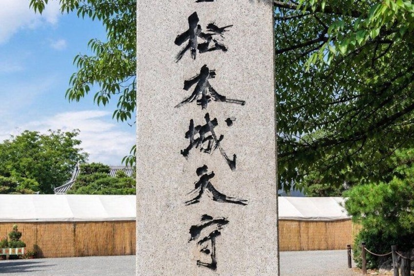 A stone monument with Chinese characters, surrounded by trees and a building in the background. 2