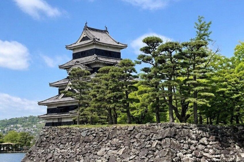 A traditional Japanese castle with multiple tiers, surrounded by lush greenery and a stone wall. 1