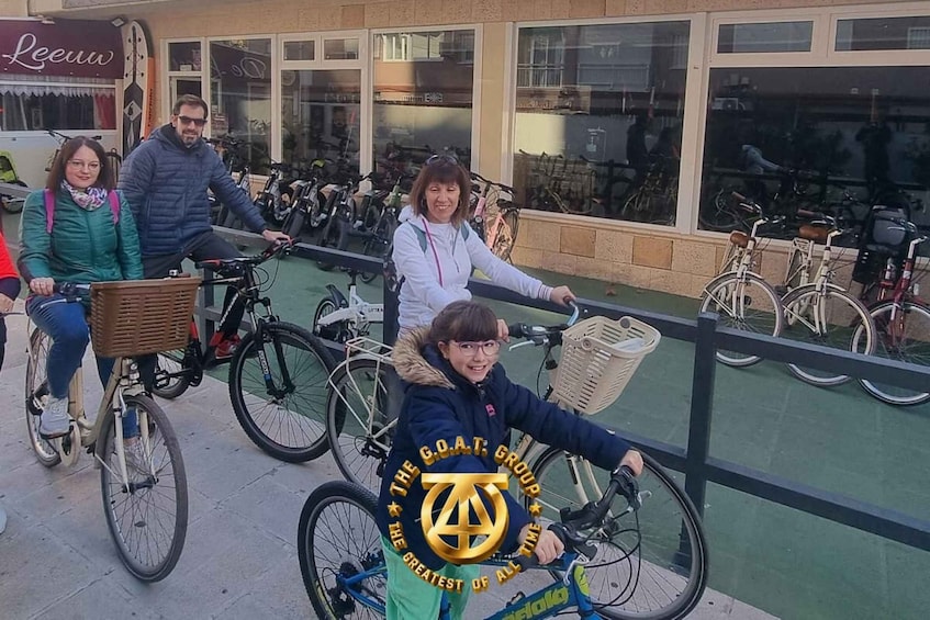 A group of people riding bicycles on a paved path with a railing on one side and a building with large windows in the background. 3